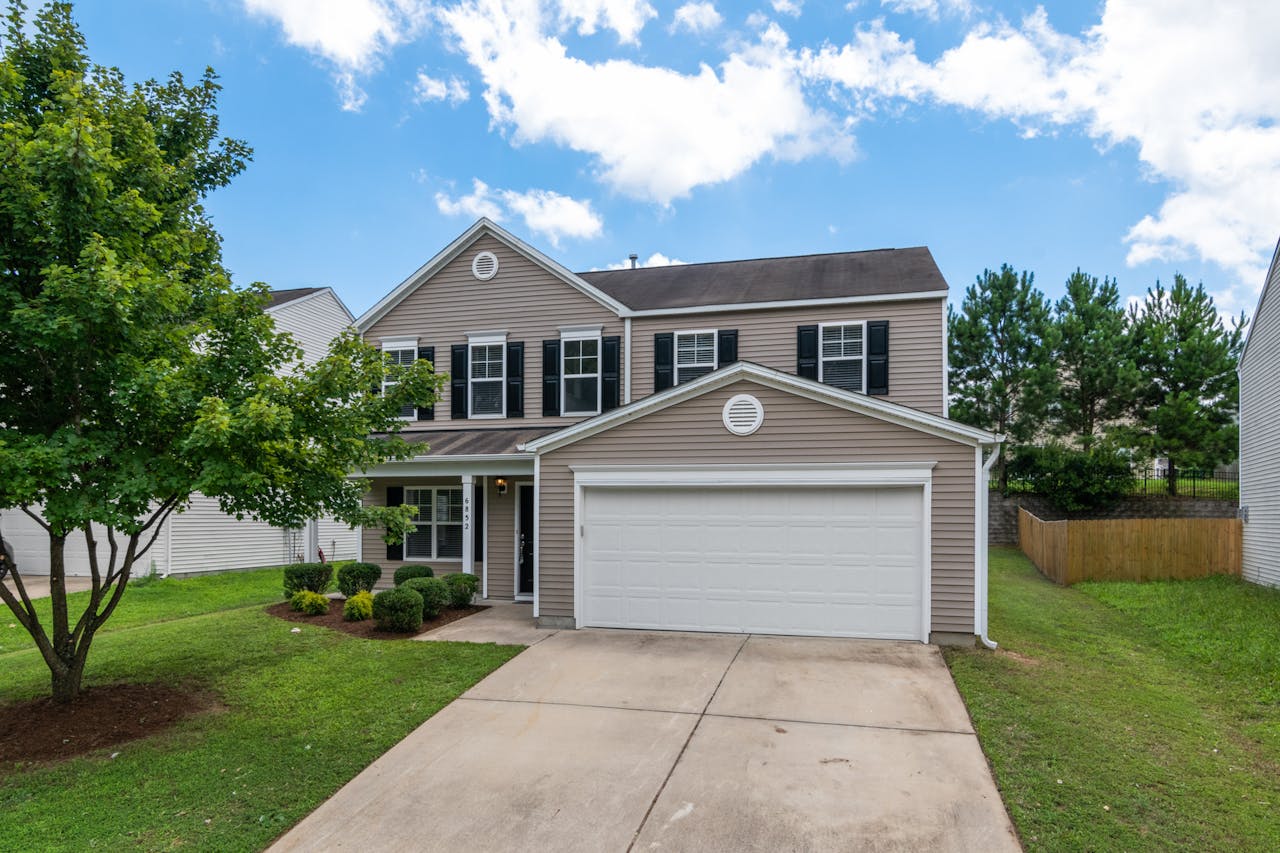 services-03 Charming two-story suburban home with green lawn, two-car garage, and blue sky.